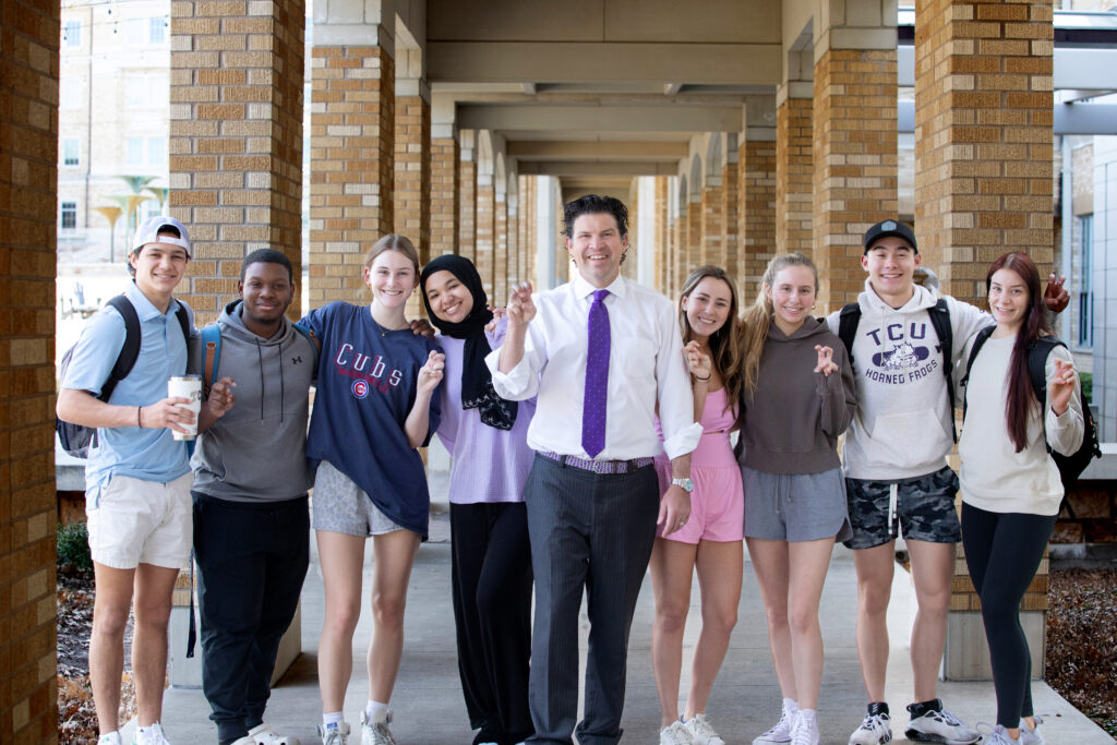 President Pullin makes the Go Frogs hand sign with a group of TCU students in the Campus Commons